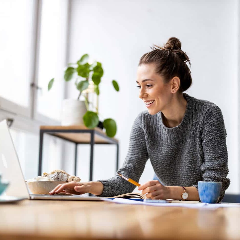 Woman smiling while working on a WordPress website on her laptop in a bright room with food nearby.