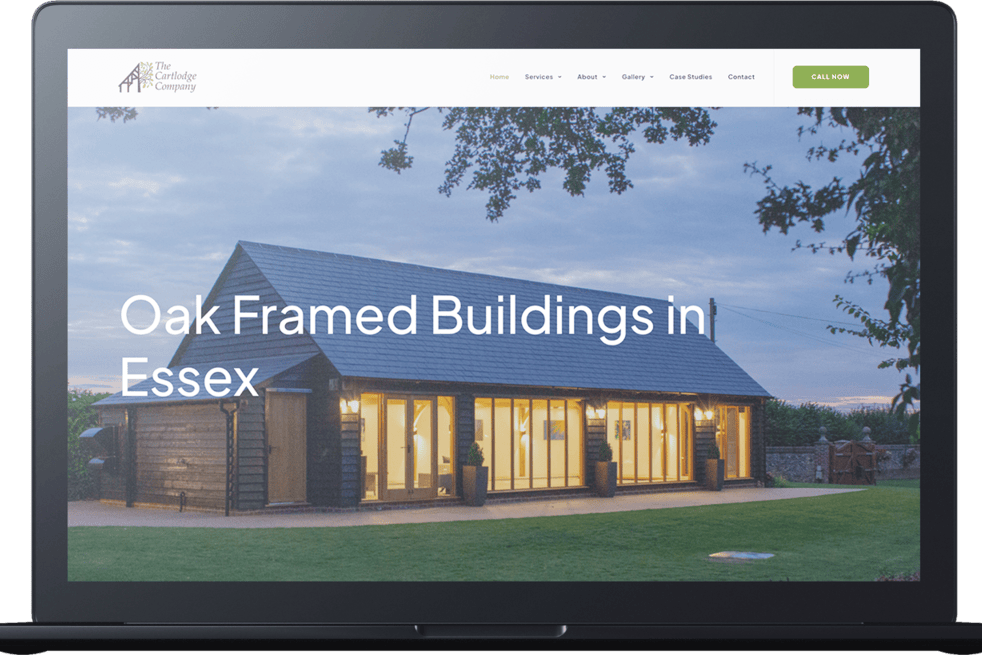 A laptop displays a website featuring a modern oak-framed building with large windows and exterior lighting, titled “Oak Framed Buildings in Essex” by a leading cart lodge company.