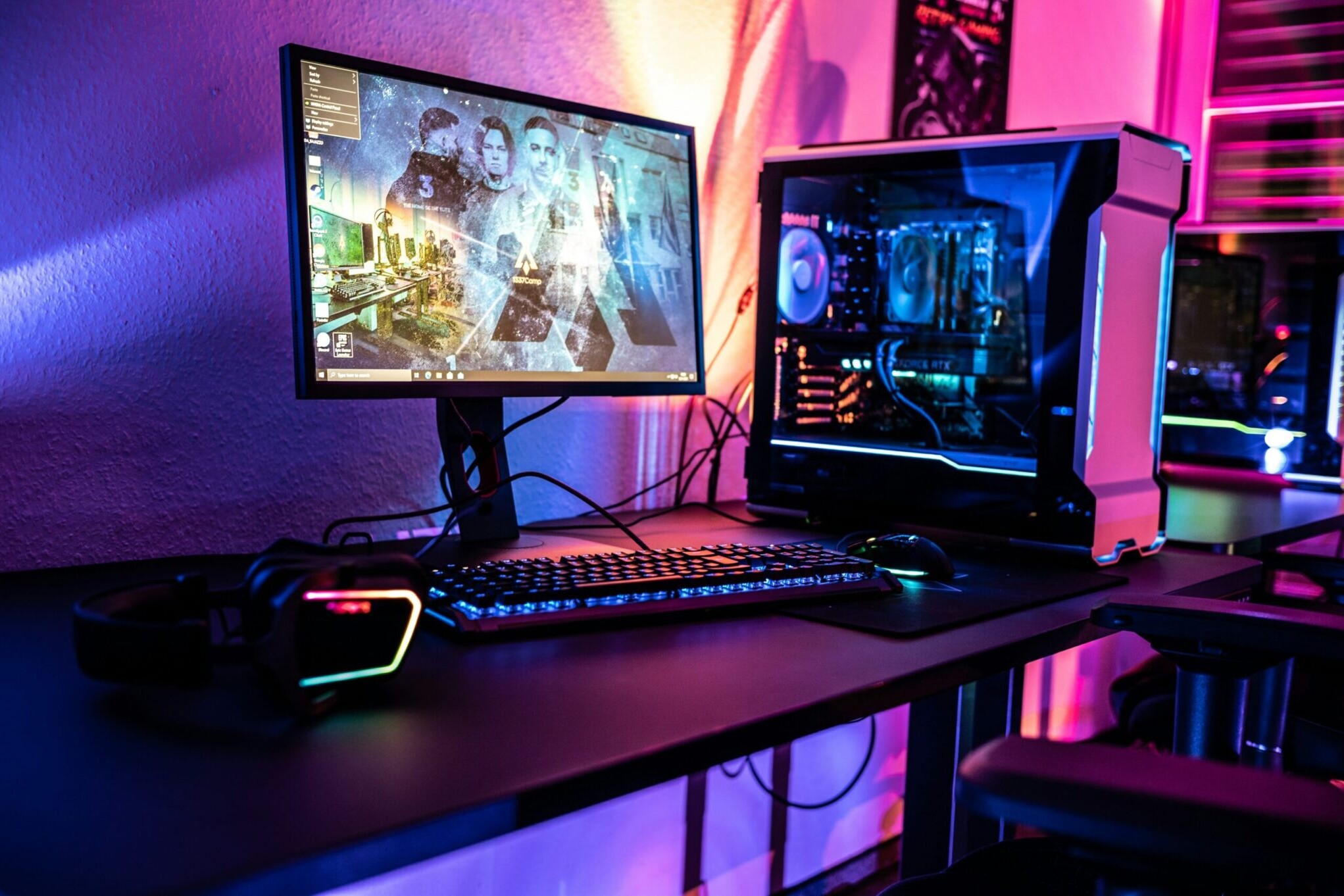 A modern gaming computer setup with a monitor displaying a game, a mechanical keyboard, mouse, headset, and a desktop PC with RGB lighting on a black desk—perfectly maintained thanks to Hardy Repairs.