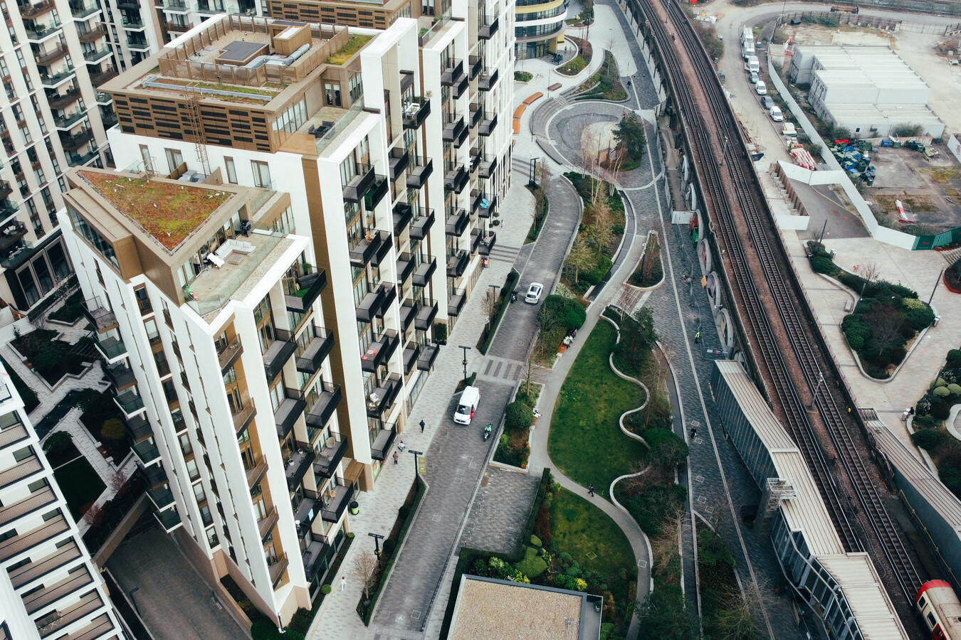 Aerial view of modern apartment buildings, landscaped walkways, a train track, and an adjacent construction site managed by Avis Contracts in a bustling urban area.