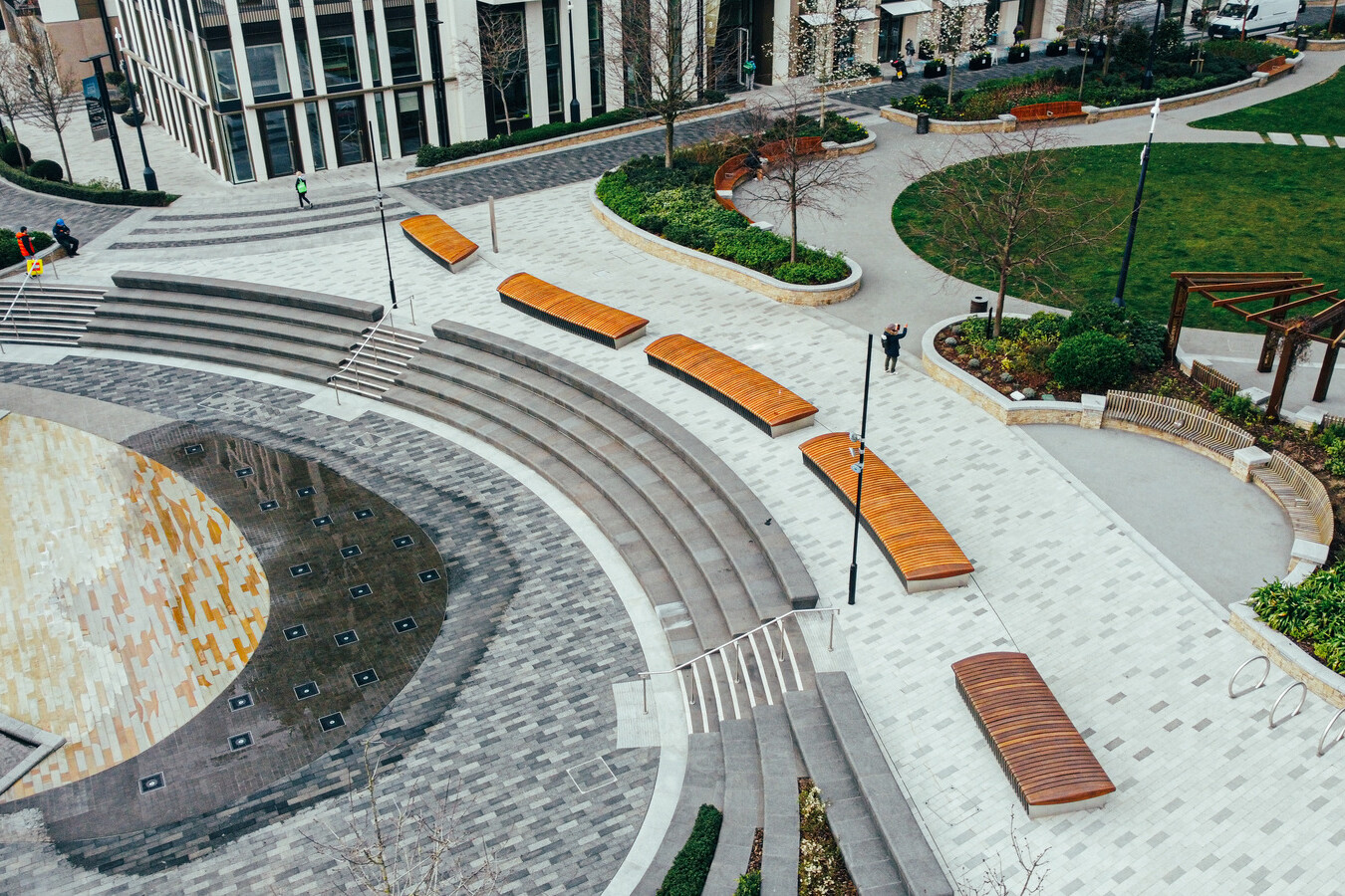 Aerial view of a modern urban plaza with curved steps, wooden benches, landscaped greenery, and paved walkways—perfectly designed for vibrant gatherings or casual meetings over Avis Contracts.