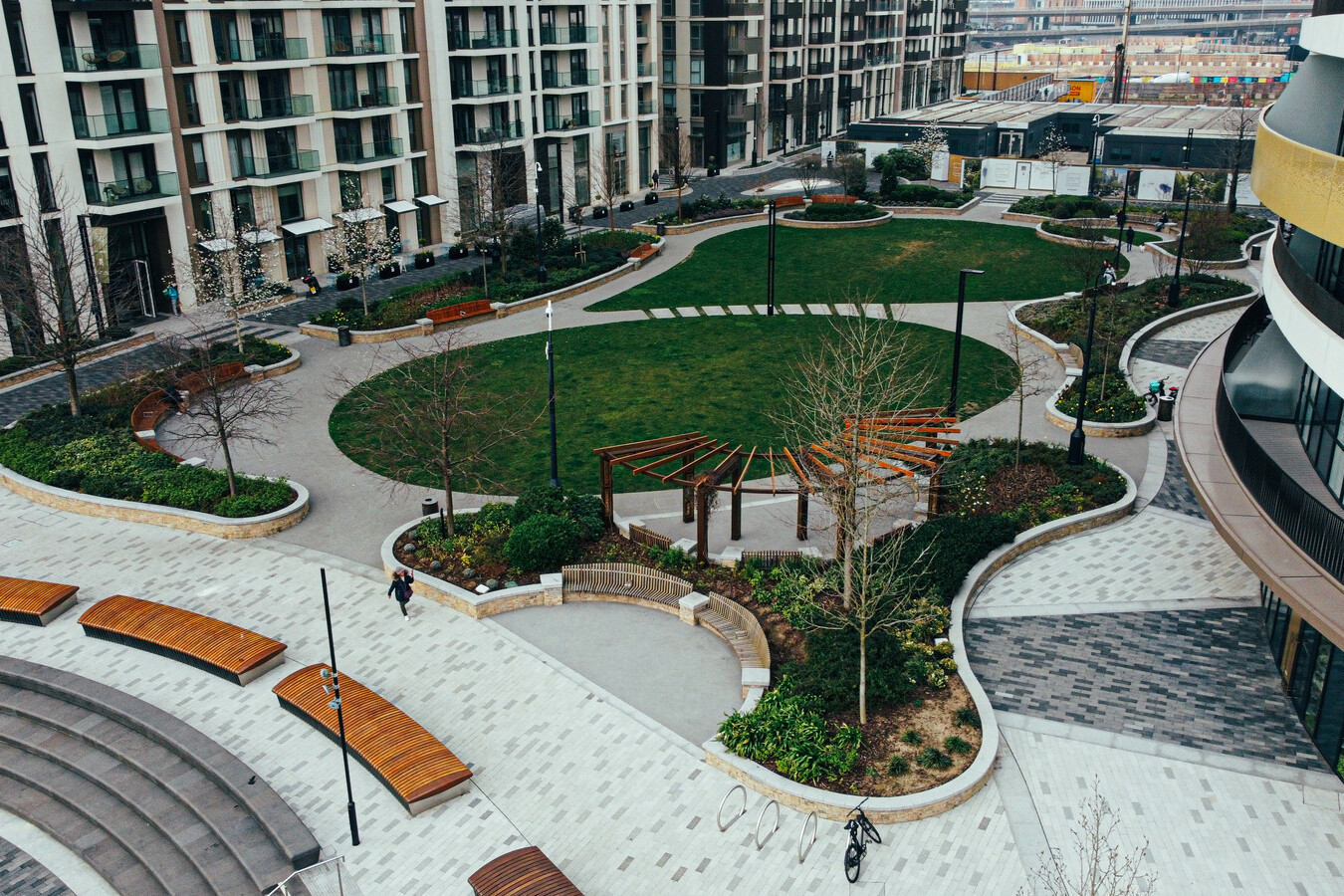 A modern urban courtyard with a central grassy area, benches, walking paths, landscaped gardens, and surrounding apartment buildings—ideal for residents and professionals managing Avis Contracts nearby.