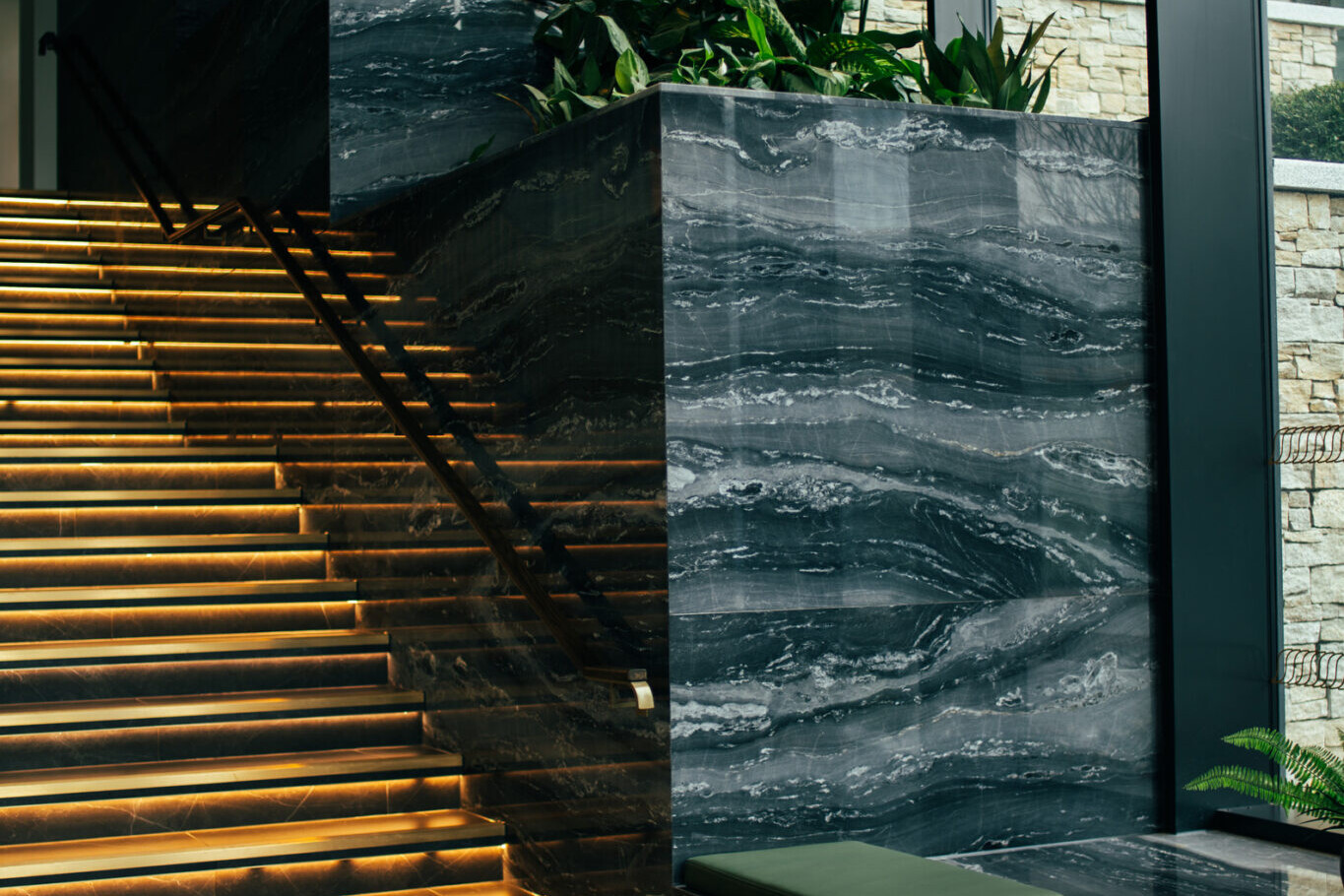 A modern interior features illuminated steps, large marble planters with green plants, and floor-to-ceiling windows letting in natural light—perfect for welcoming clients or discussing Avis Contracts in style.